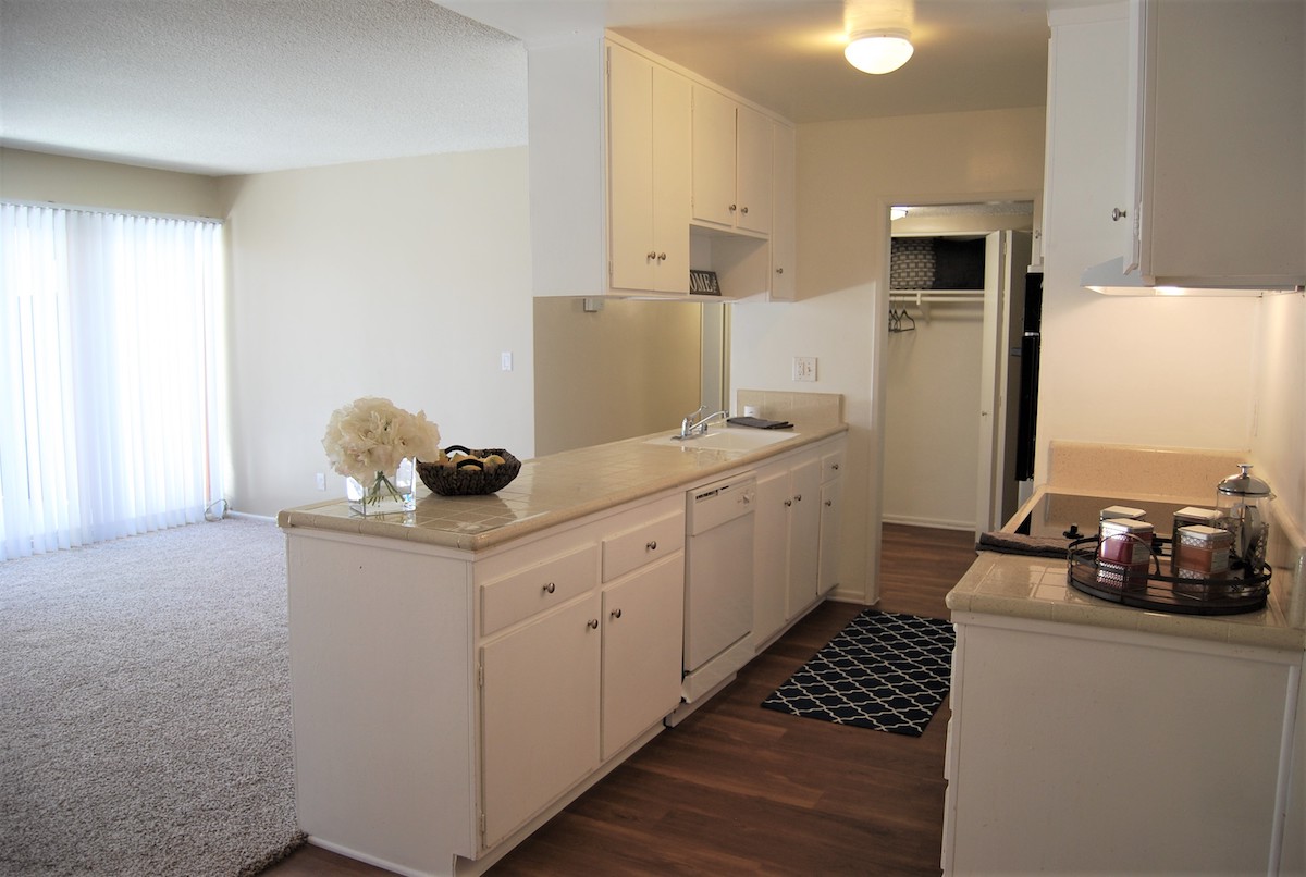 Kitchen featuring porcelain countertops, overhead cabinets, wood-inspired flooring and contemporary appliances.