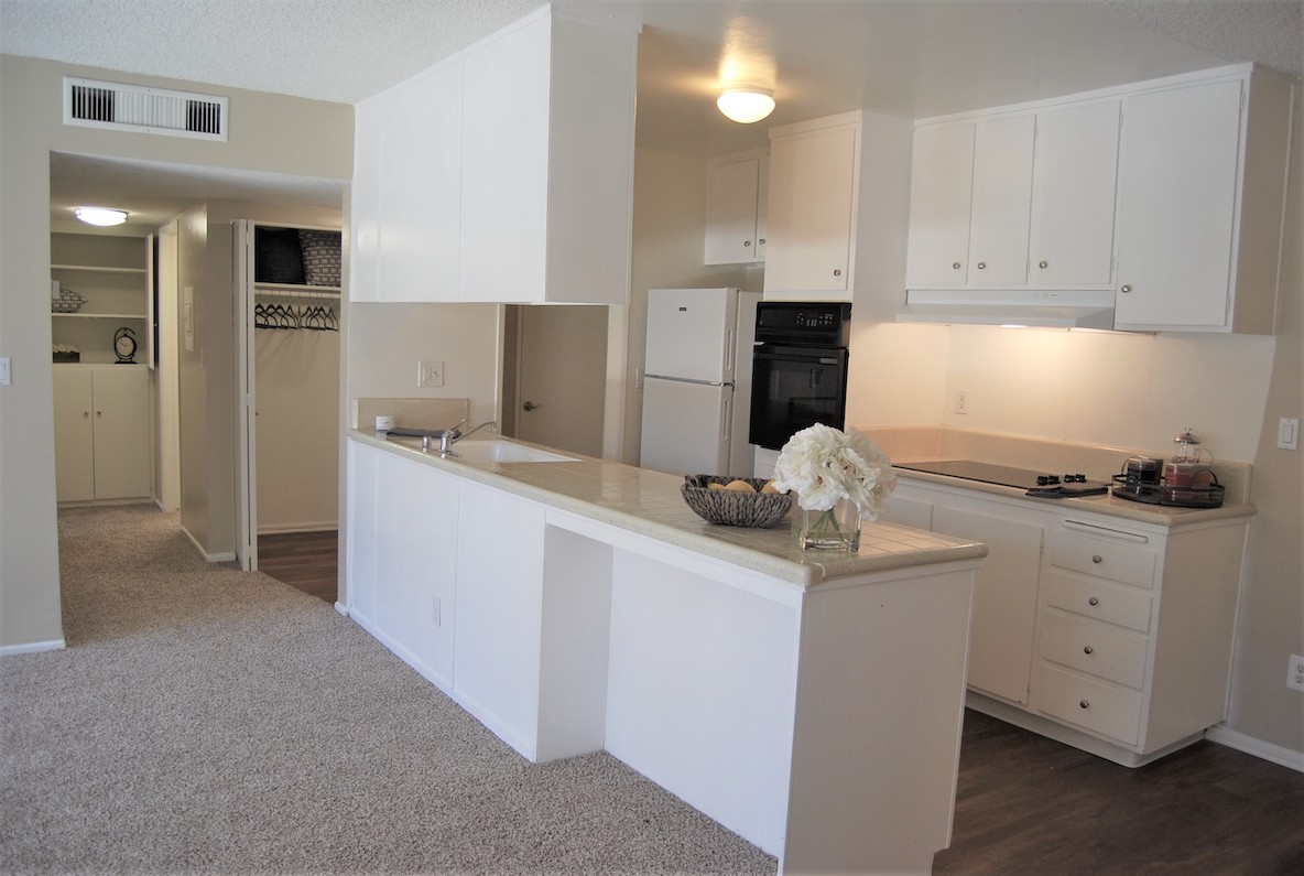 Apartment living room looking towards the kitchen featuring porcelain countertops, overhead cabinets and contemporary appliances.